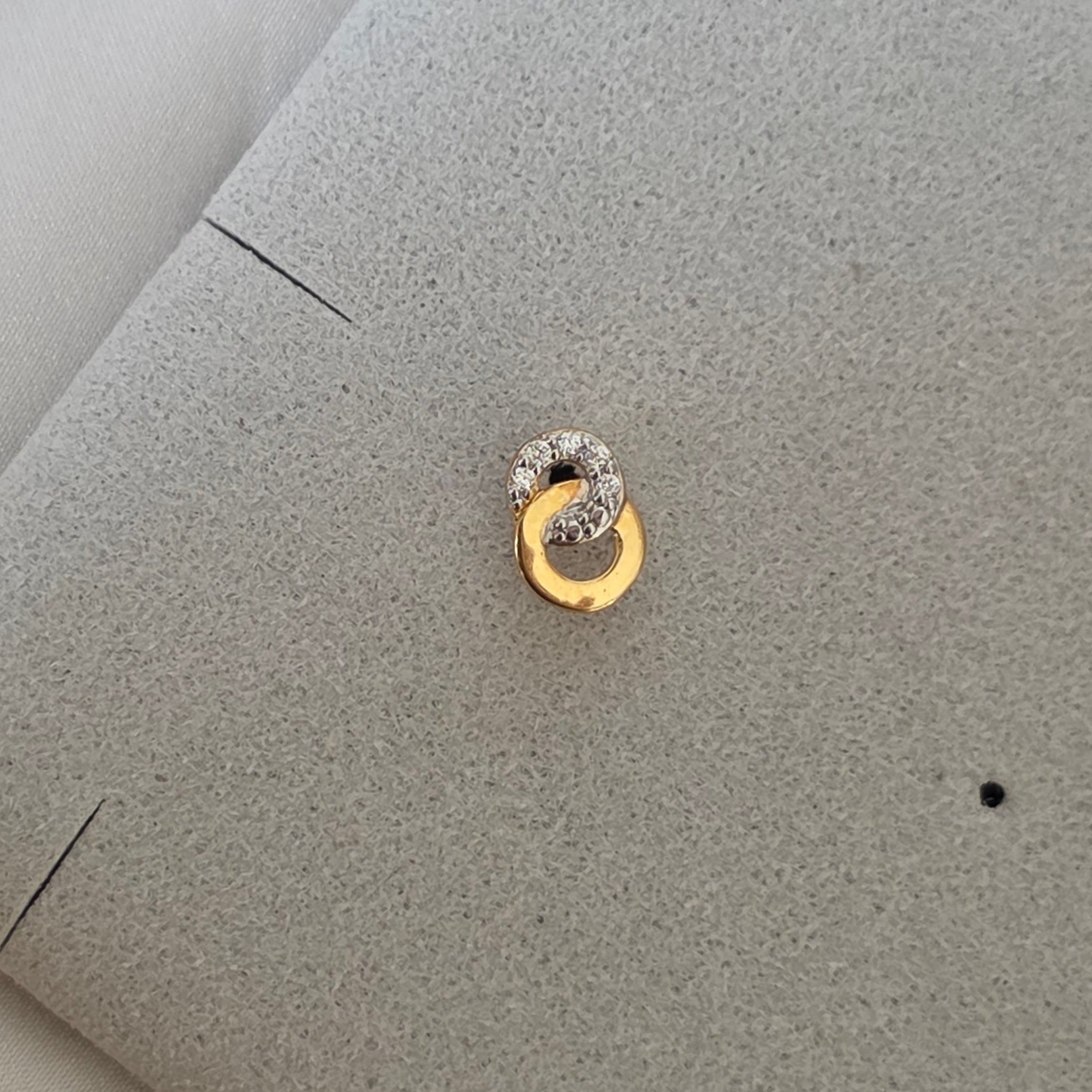 Puce d'oreille Carelle posée à plat, deux anneaux dorés entrelacés vus de face