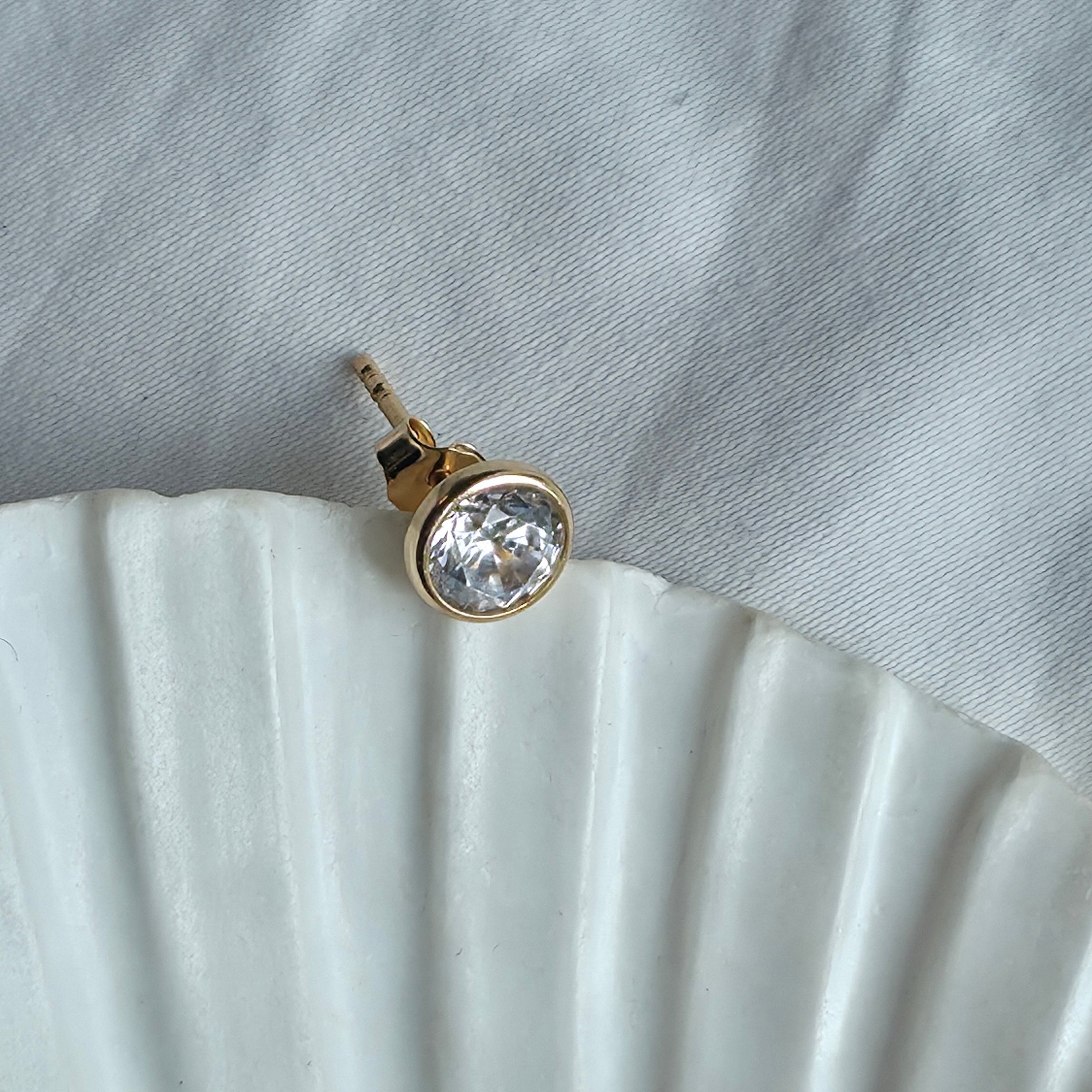 Puce d'oreille solitaire zircon rond et monture dorée posée sur fond clair