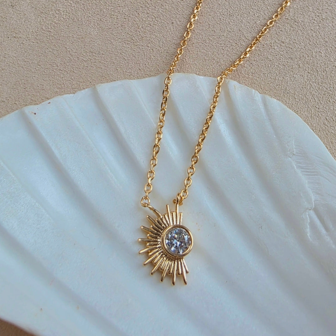 Bijou Orphé en plaqué or en forme de demi-soleil, orné d’un cristal central, photographié en lumière naturelle sur fond neutre.