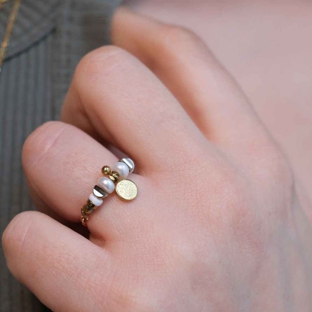 Bague fine en perles nacrées, hématite sombre et coquillage naturel, bijou symbolisant l’équilibre entre douceur et structure.