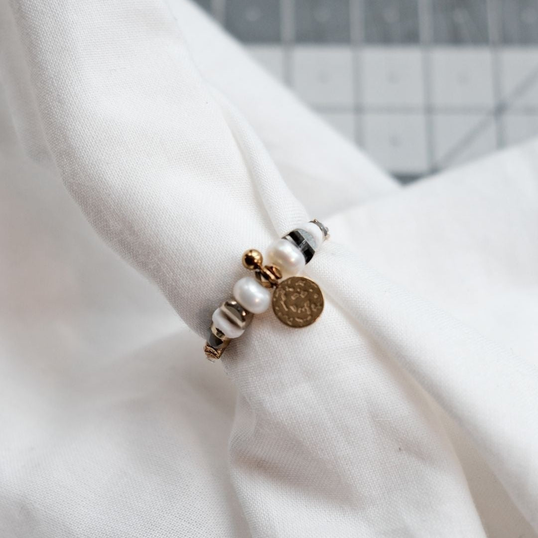 Bague artisanale en perles naturelles avec hématite brillante et coquillage clair, inspirée de l’énergie marine et féminine.